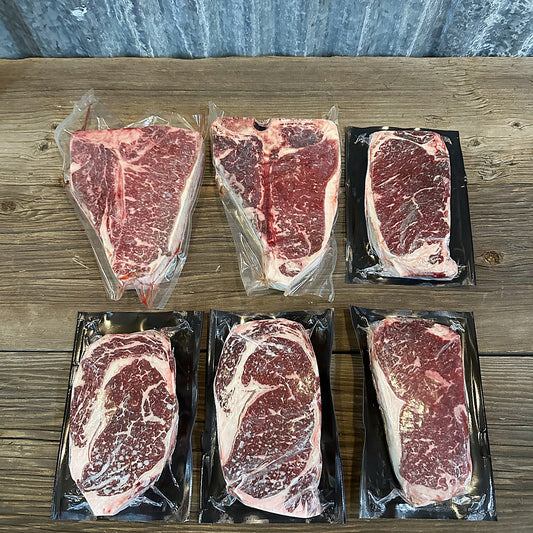 Two T-bone steaks, two ribeyes and two New York strips on a wood table