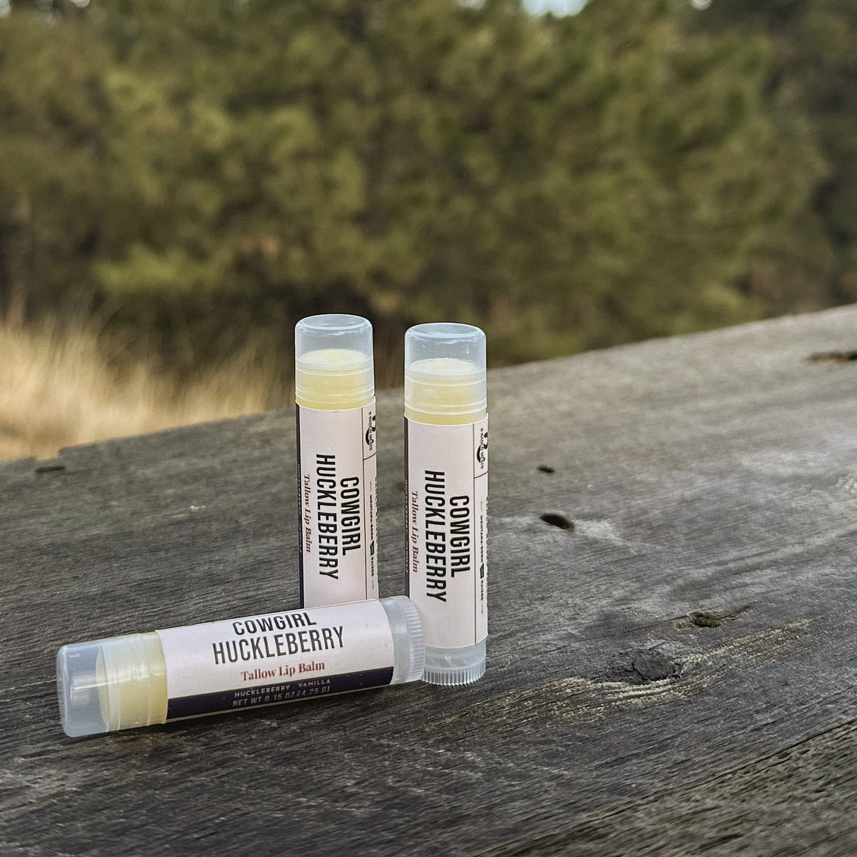 Three tubes of Cowgirl Huckleberry tallow lip balm on a weathered ranch table in Montana