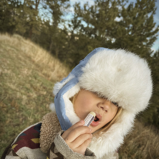 Ranch kid in a fur trapper hat putting on Cowgirl Huckleberry tallow lip balm