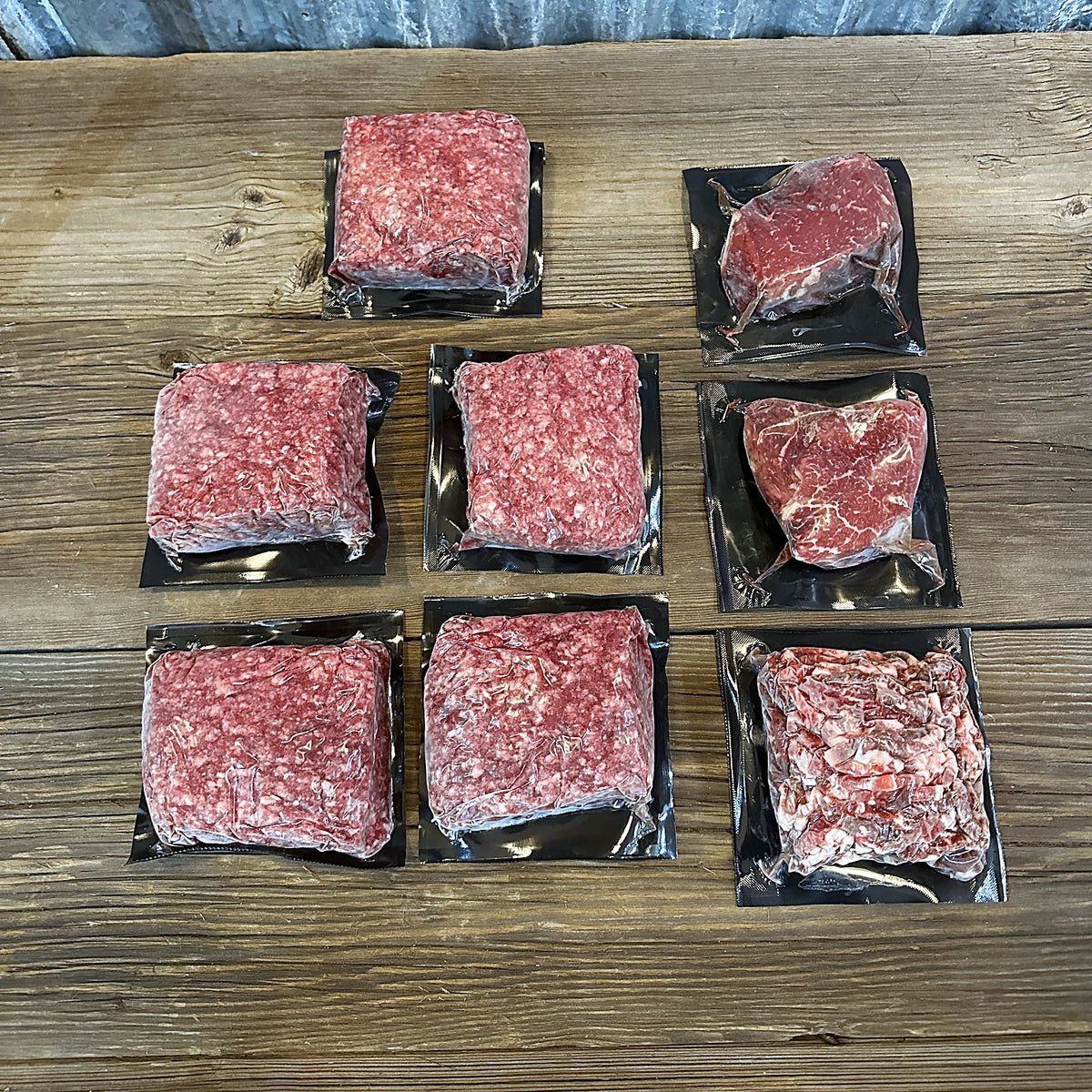 Two sirloin steaks, five 1 lb packs of ground beef and carne picada laid out on a wood table