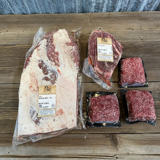 Whole packer brisket, chuck roast and three packs of ground beef on a wood table