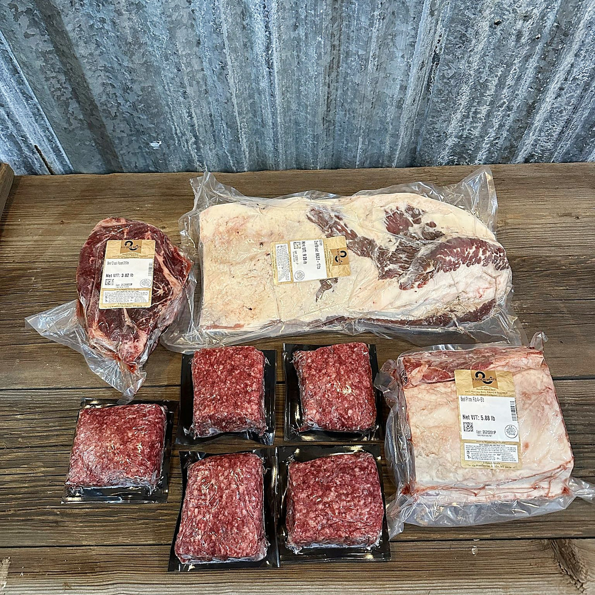 Prime rib roast, whole brisket, chuck roast and five packs of ground beef on a wood table