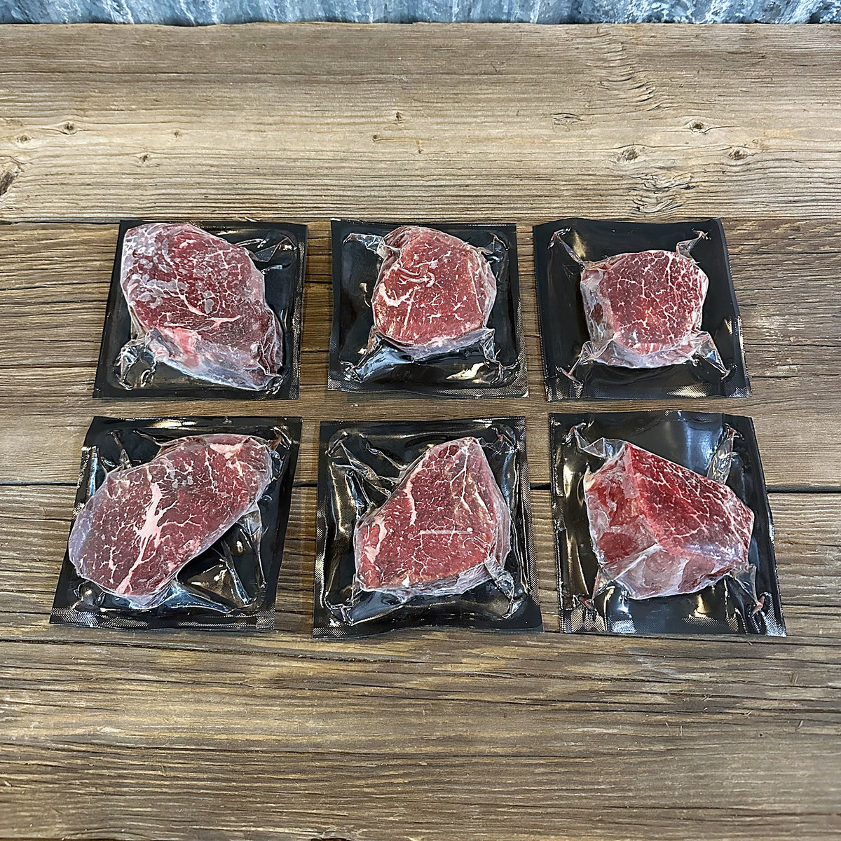 Six filet mignon steaks, two each at 6, 8 and 10 oz, on a wood table