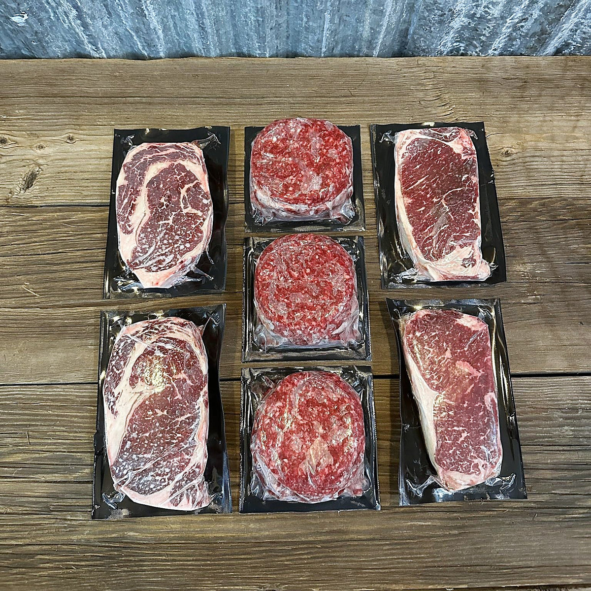 Two ribeyes, two New York strips and three packs of burger patties on a wood table