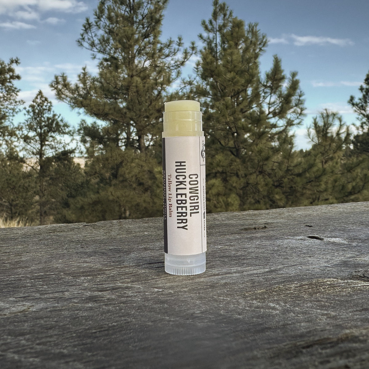 Cowgirl Huckleberry tallow lip balm tube standing on a ranch table under ponderosa pines