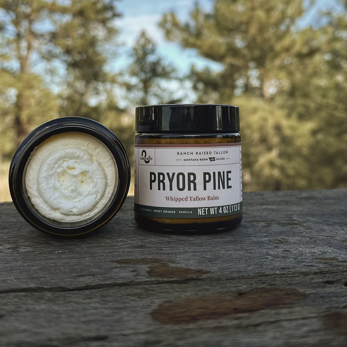 Pryor Pine tallow balm jar on a ranch table with ponderosa pines behind