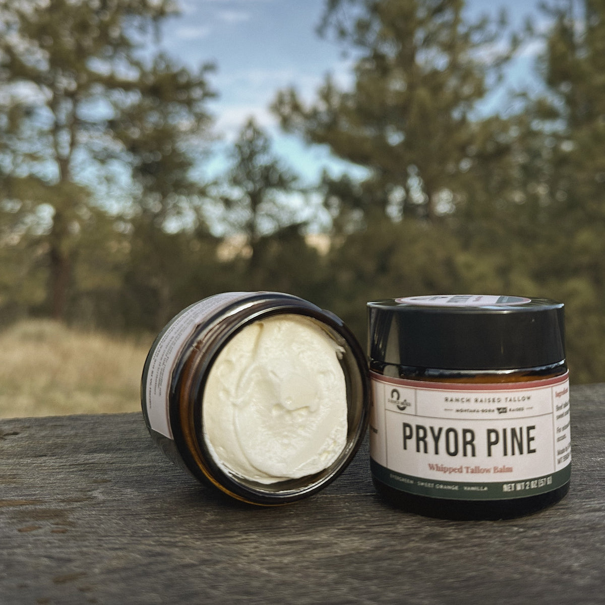 Pryor Pine 2 oz mini whipped tallow balm, open jar beside the labeled jar on a ranch table