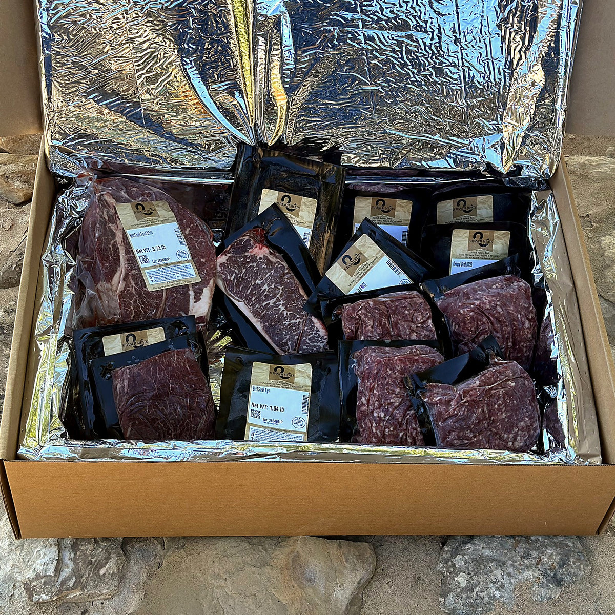 S Ranch Meats beef box open on Montana rock: vacuum-sealed steaks and ground beef in the insulated liner