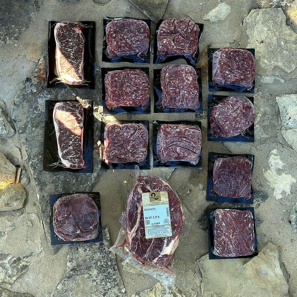 An S Ranch Meats beef box laid out: vacuum-sealed strip steaks, ground beef, sirloins and a chuck roast on Montana stone