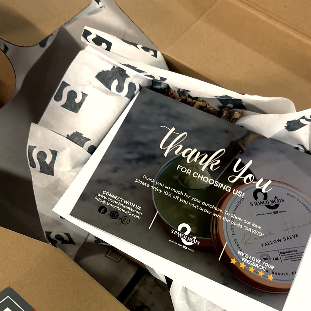 Inside an S Ranch Meats order: branded tissue paper, thank-you card and tallow salve