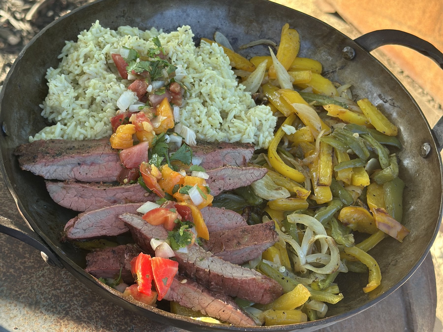 Flank steak fajitas with peppers and cilantro-lime rice in a skillet on the wood stove